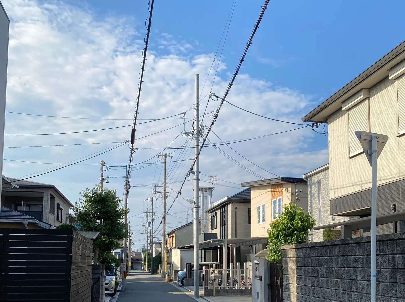 青空と電線の下、住宅が並ぶ静かな通り