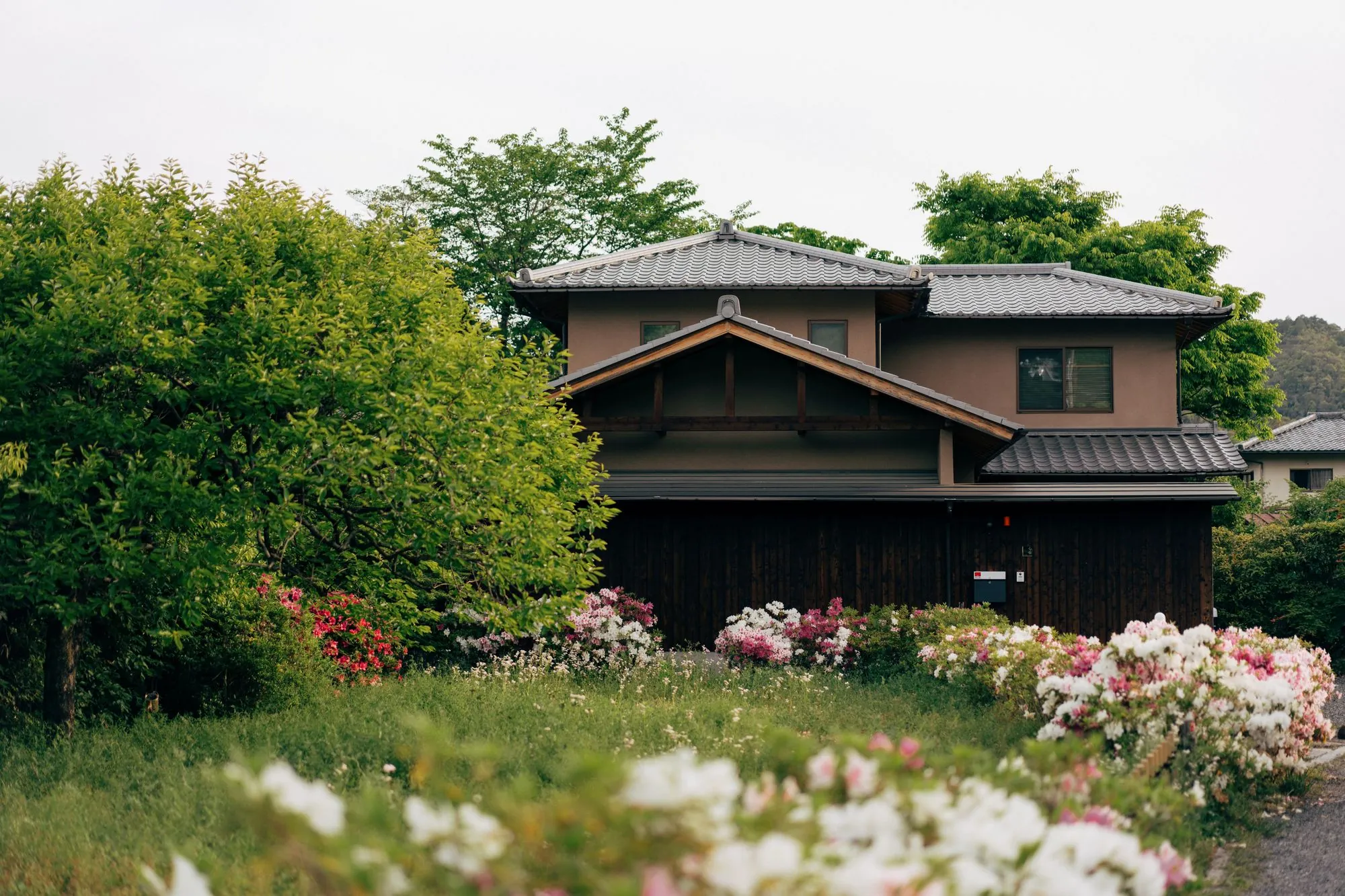 花の咲く庭と木々に囲まれた二階建ての家