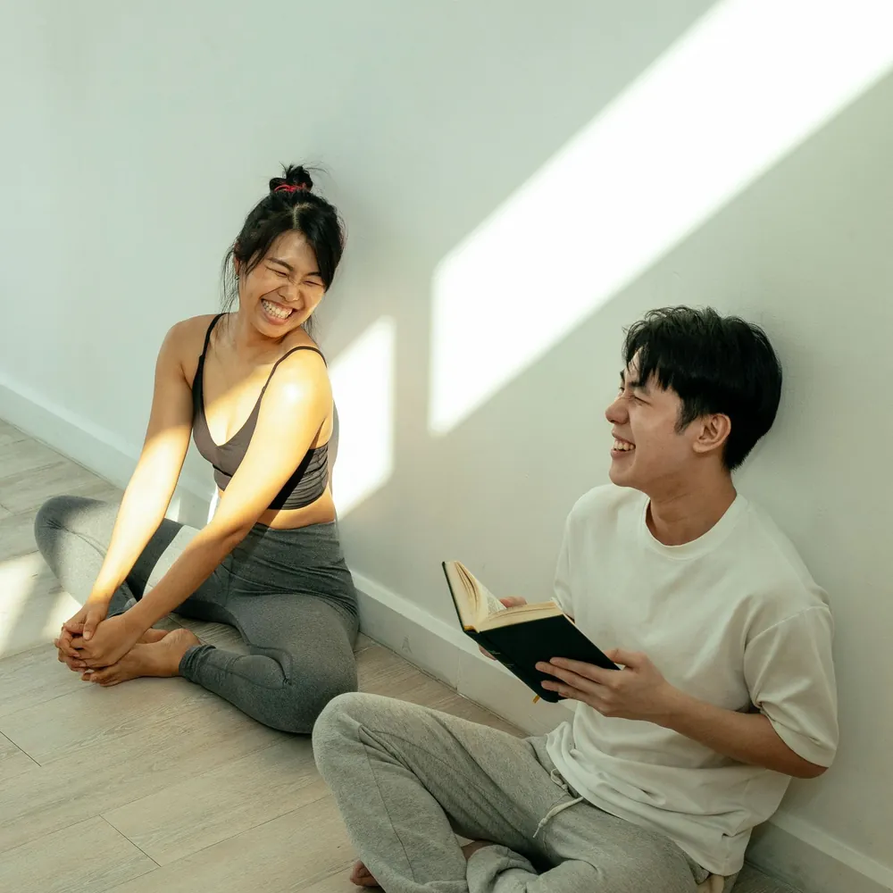 日当たりのよい部屋の床に座って笑い合う若い二人