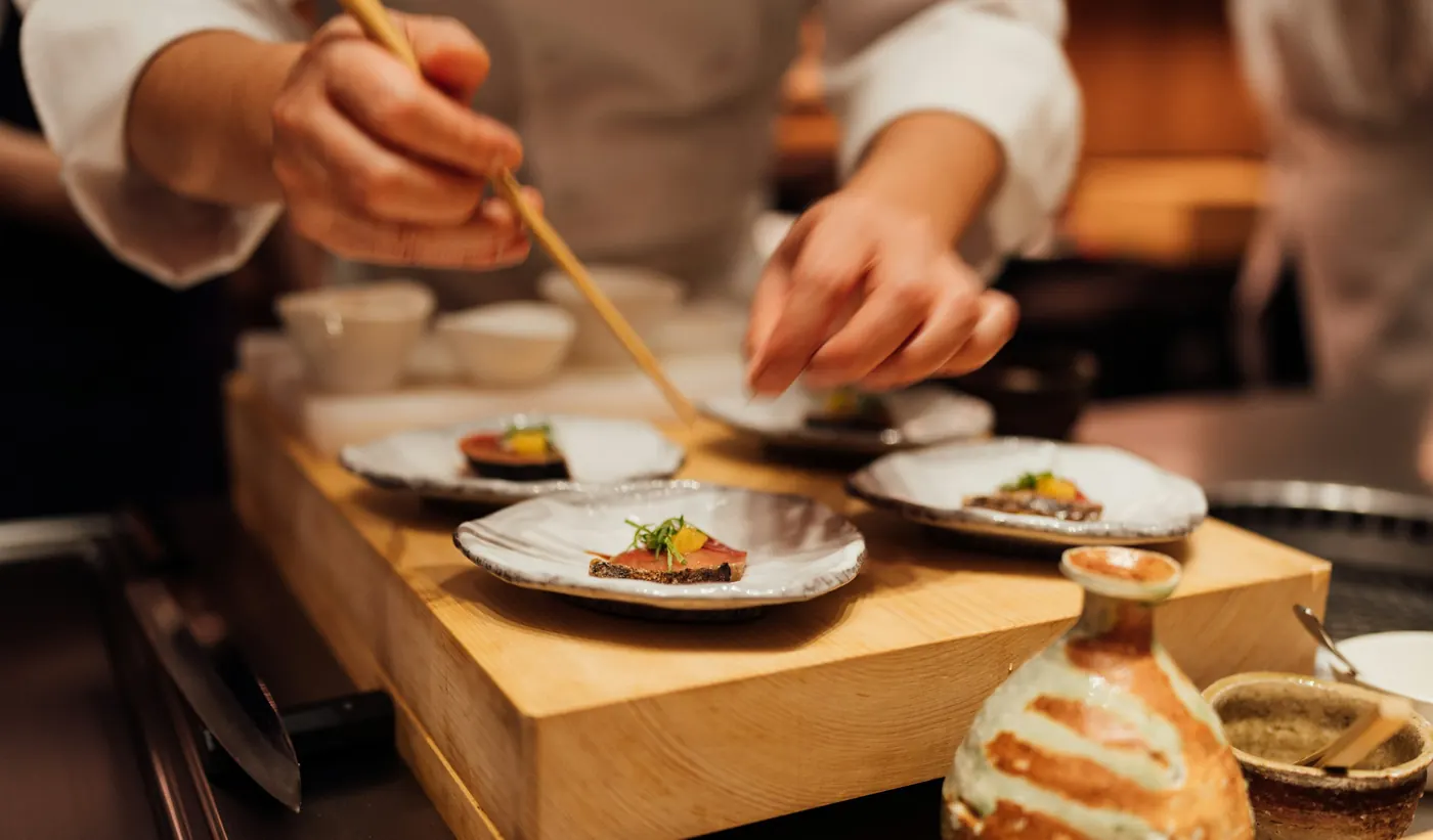 木のまな板の上で料理を盛り付ける料理人の手元