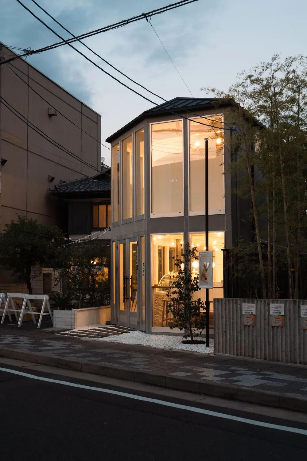 夕暮れに灯りがともるガラス張りの店舗併用住宅