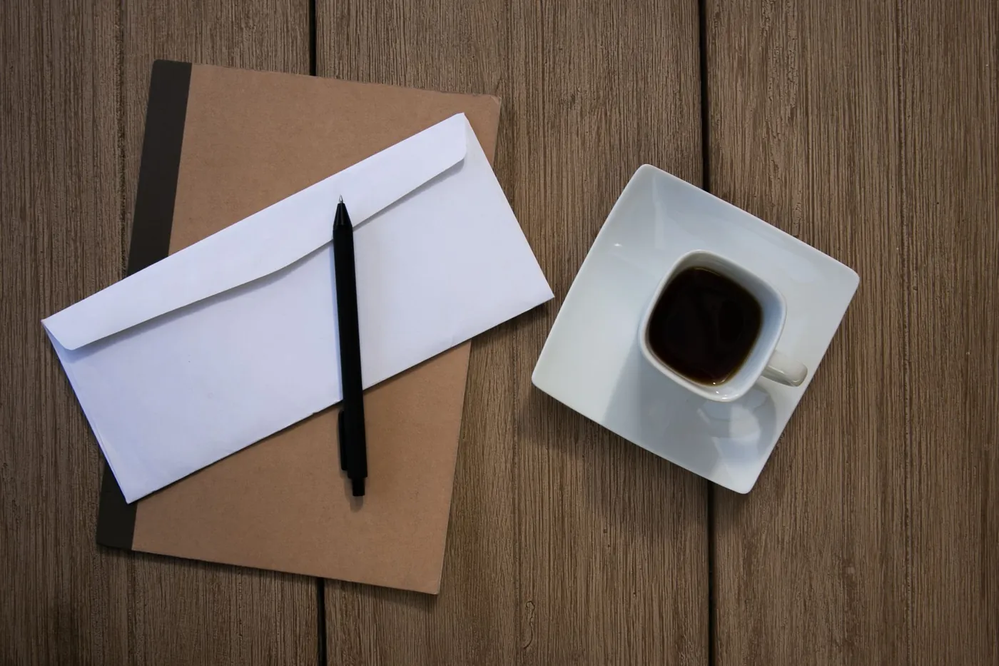 木の机に置いた茶色のノートと白い封筒、ペン、コーヒー
