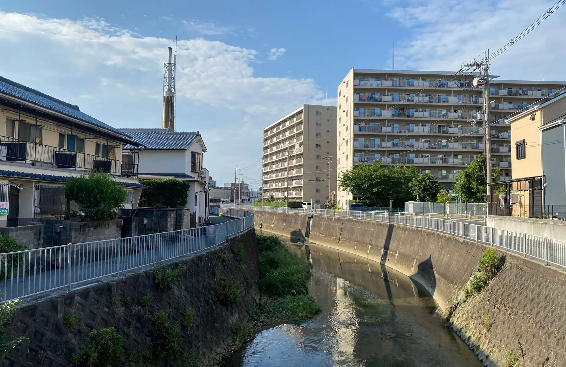 青空の下、小さな川沿いに住宅やマンションが並ぶまちの風景